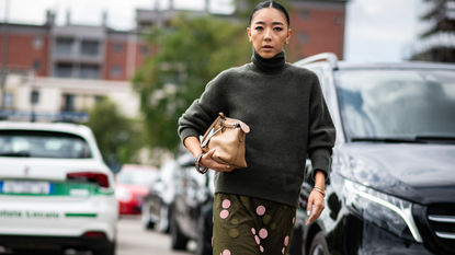 A guest attends milan spring summer 2025 fashion week wearing grey turtleneck sweater, green and pink sequin skirt, and carrying beige handbag