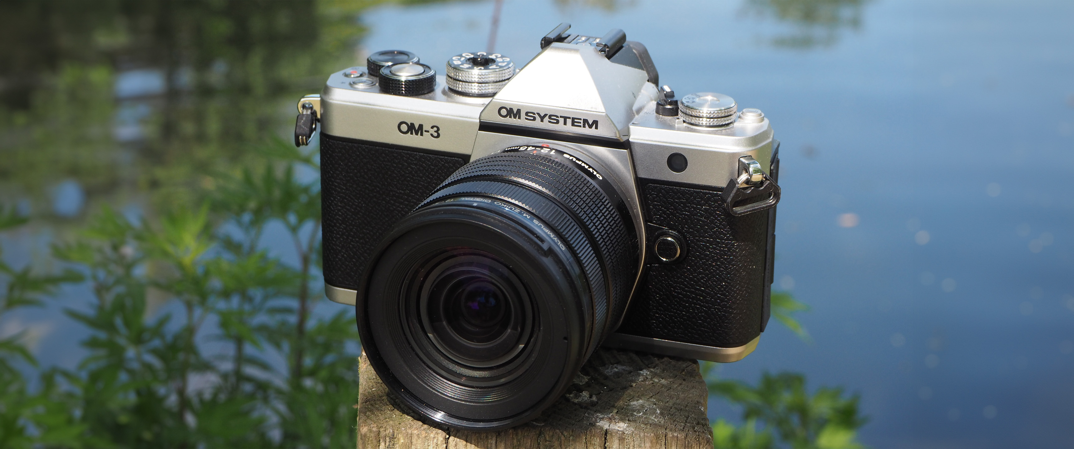 OM System OM-3 on a wooden post next to a pond