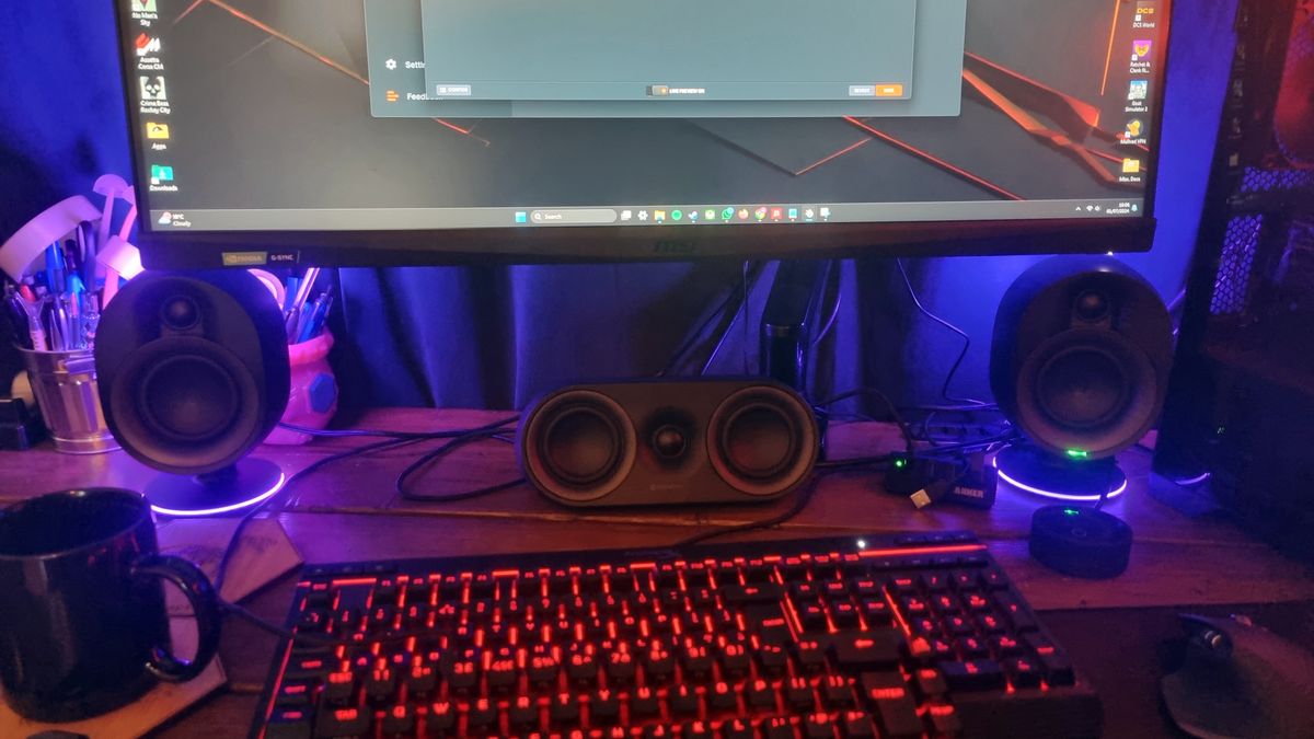 The SteelSeries Arena 9 speakers on a desktop, lit up in purple/pink, underneath a 32 inch MSI gaming monitor