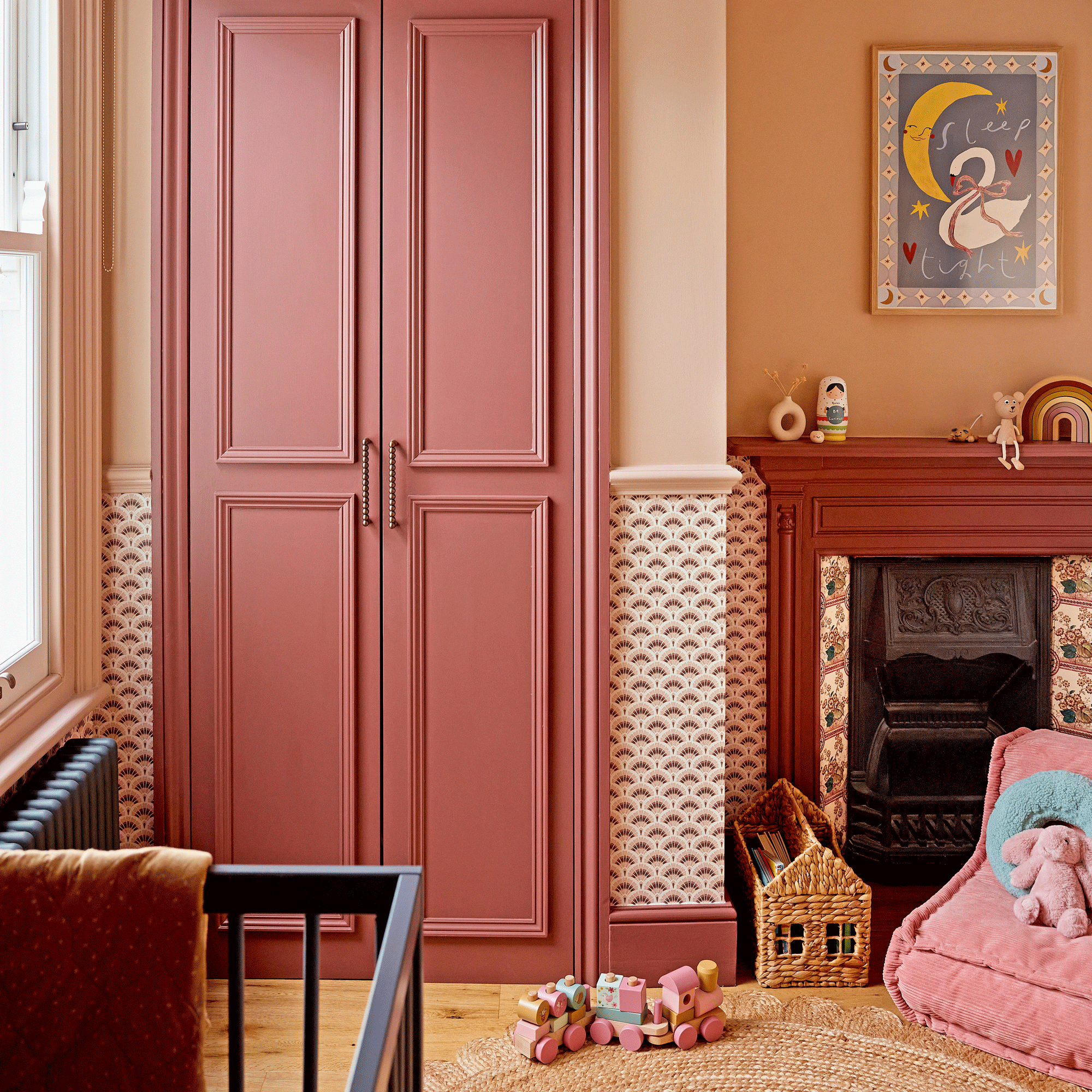 a childs bedroom with a cot, patterned wallpaper and colour drenched fitted wardrobe
