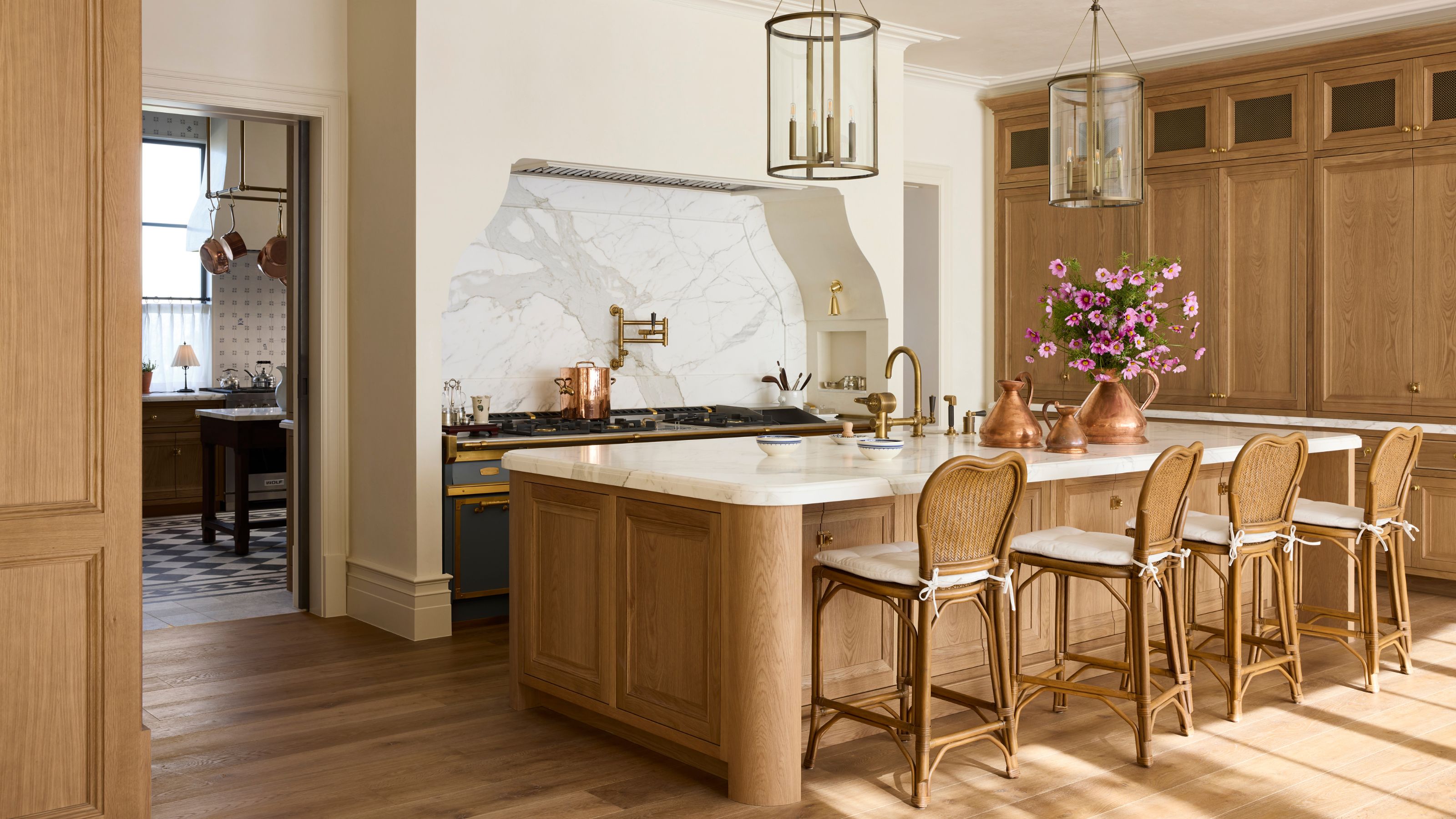 a vast oak kitchen with a large curved plaster cooker hood area with a blue rangecooker, curved kitchen island with rattan chairs and a view to a pantry