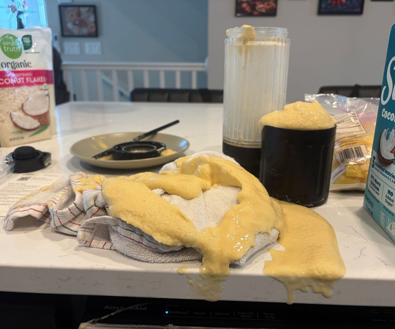 A yellow smoothie all over a towel on a counter, with a small blender behind it.