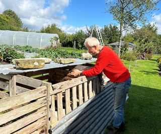 Charles Dowding holding some compost by his compost bins