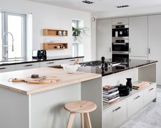 Modern kitchen with large kitchen island, countertop in light wood and black Antique Natural Stone, pale gray cupboards and white painted walls, light wood, rounded stool