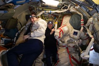 Pyotr Dubrov (left) and Oleg Novitskiy prepare Russian Orlan spacesuits inside the International Space Station's Poisk module.