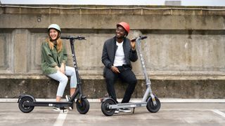 Man and woman sitting on a bench, each with a Pure Air Pro electric scooter