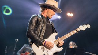 Kenny Wayne Shepherd plays his signature Fender Stratocaster capo'd at the second fret during a 2024 performance at Los Angeles' Shrine Auditorium and Expo Hall. He wears a wide-brimmed hat, black leather jacket and black T-shirt.