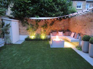 outdoor living space at night with built in sofa with fire, festoon lights and a sail shade