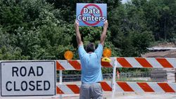 Man protesting data centers next to a road closed sign.