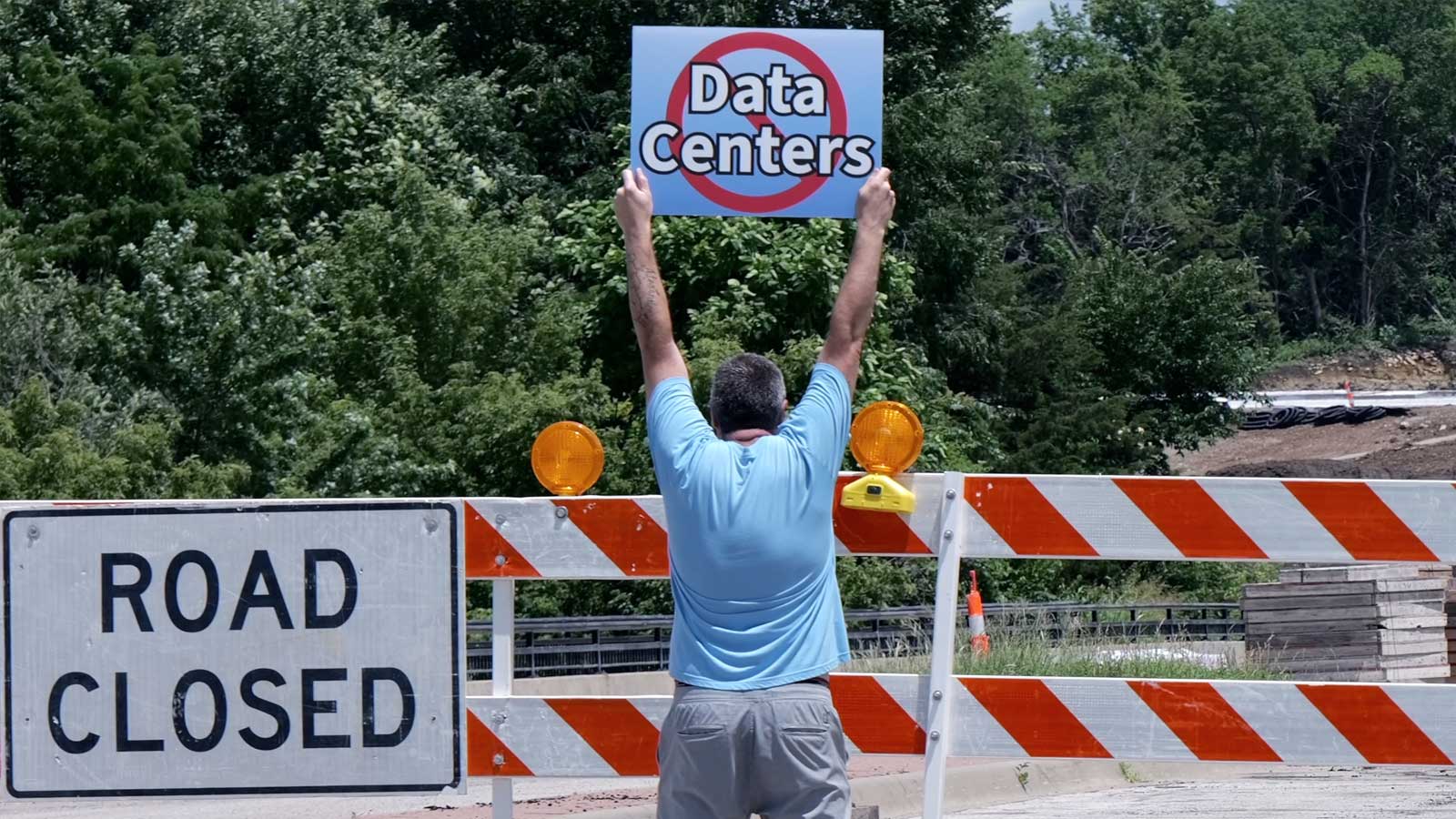 Man protesting data centers next to a road closed sign.