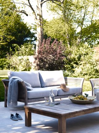 cream outdoor sofa in a garden seating area, with a wooden table on a paved section of garden