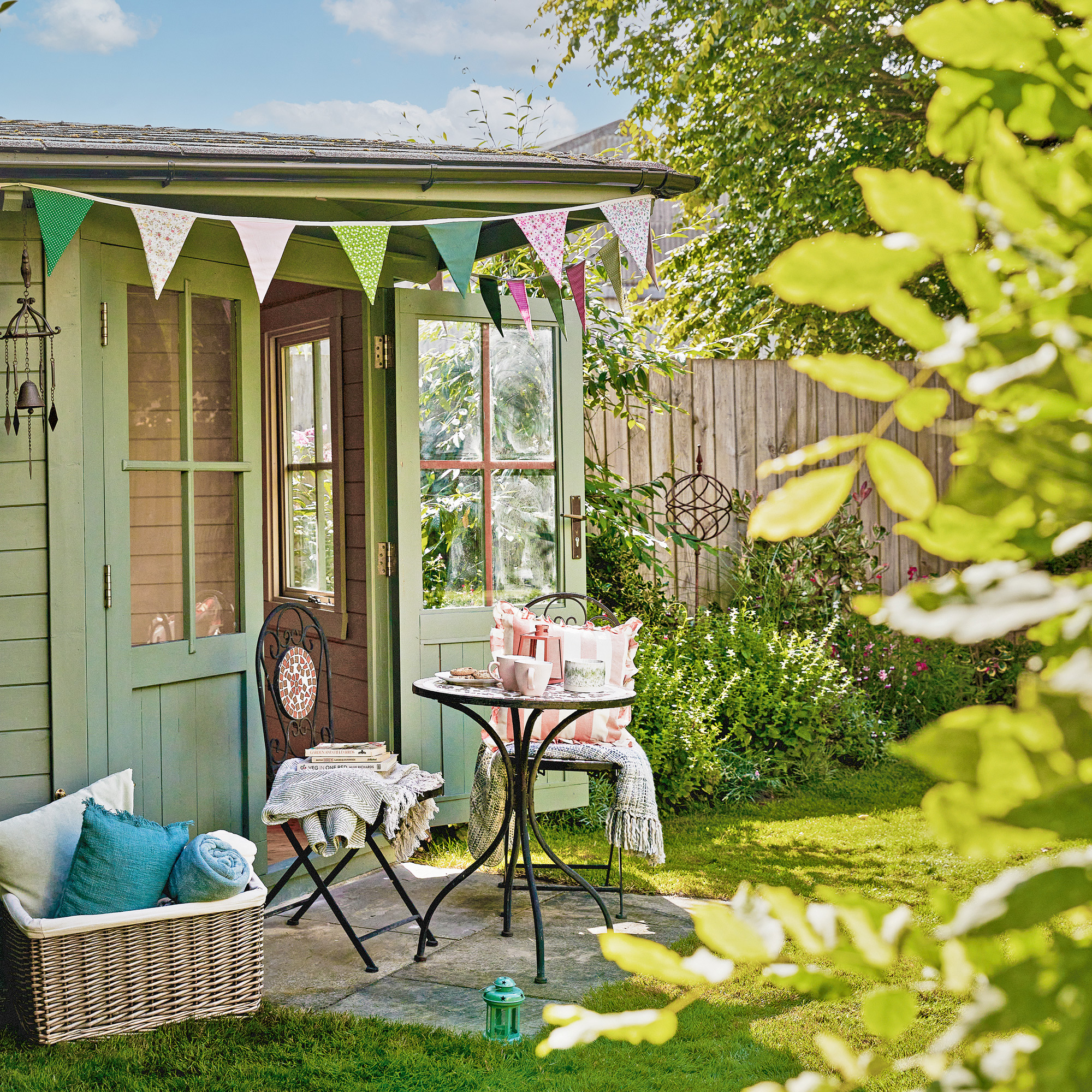 a green painted summerhouse decorated with colourful bunting and a bistro table and chairs