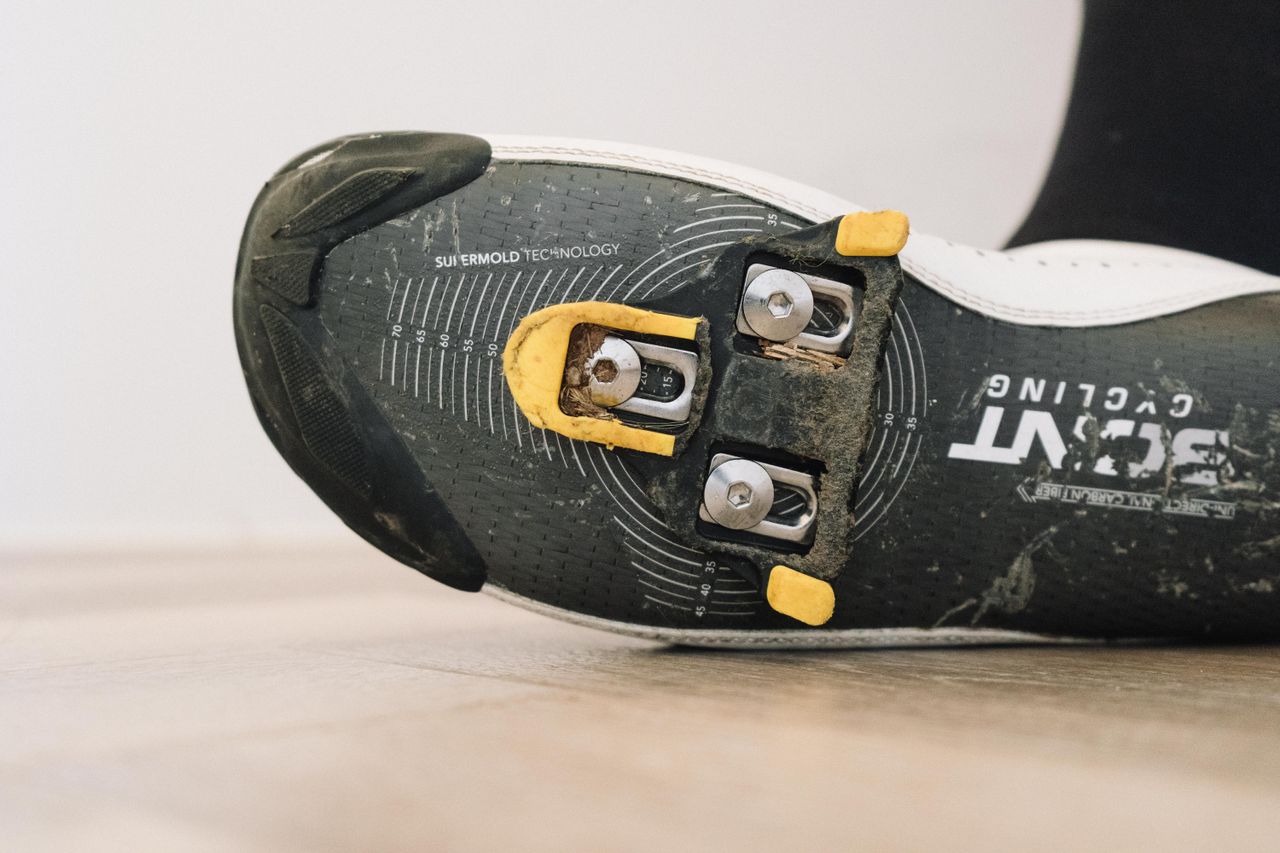 A close up of a white cycling shoe with a black socked foot in it