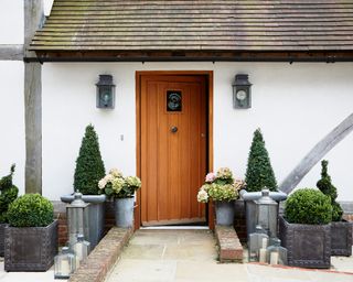 A front porch with a wooden door and two wall lights behind plant pots