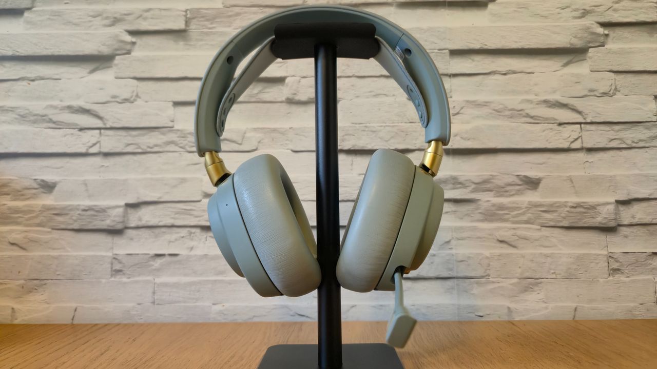 The SteelSeries Arctis Nova Elite headset in front of a white brick background and on a wooden surface
