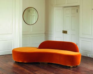 Julian Chichester orange curved velvet sofa on wooden floor with panelled walls