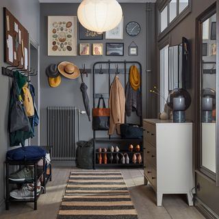 a busy hallway with framed pictures on the wall alongside a coat stand, storage bench and chest of drawers