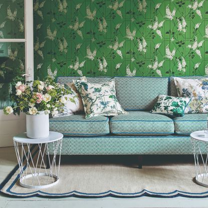 A living room with a green floral wallpaper with a patterned sofa in front of it with contrasting blue piping