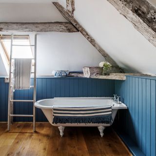 attic bathroom with wooden floor and bathtub and white and blue wall and ladder towel rack