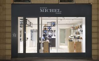 The front of a Maison Michel store with a thick black frame with the logo on it surrounding the doorway and large window.