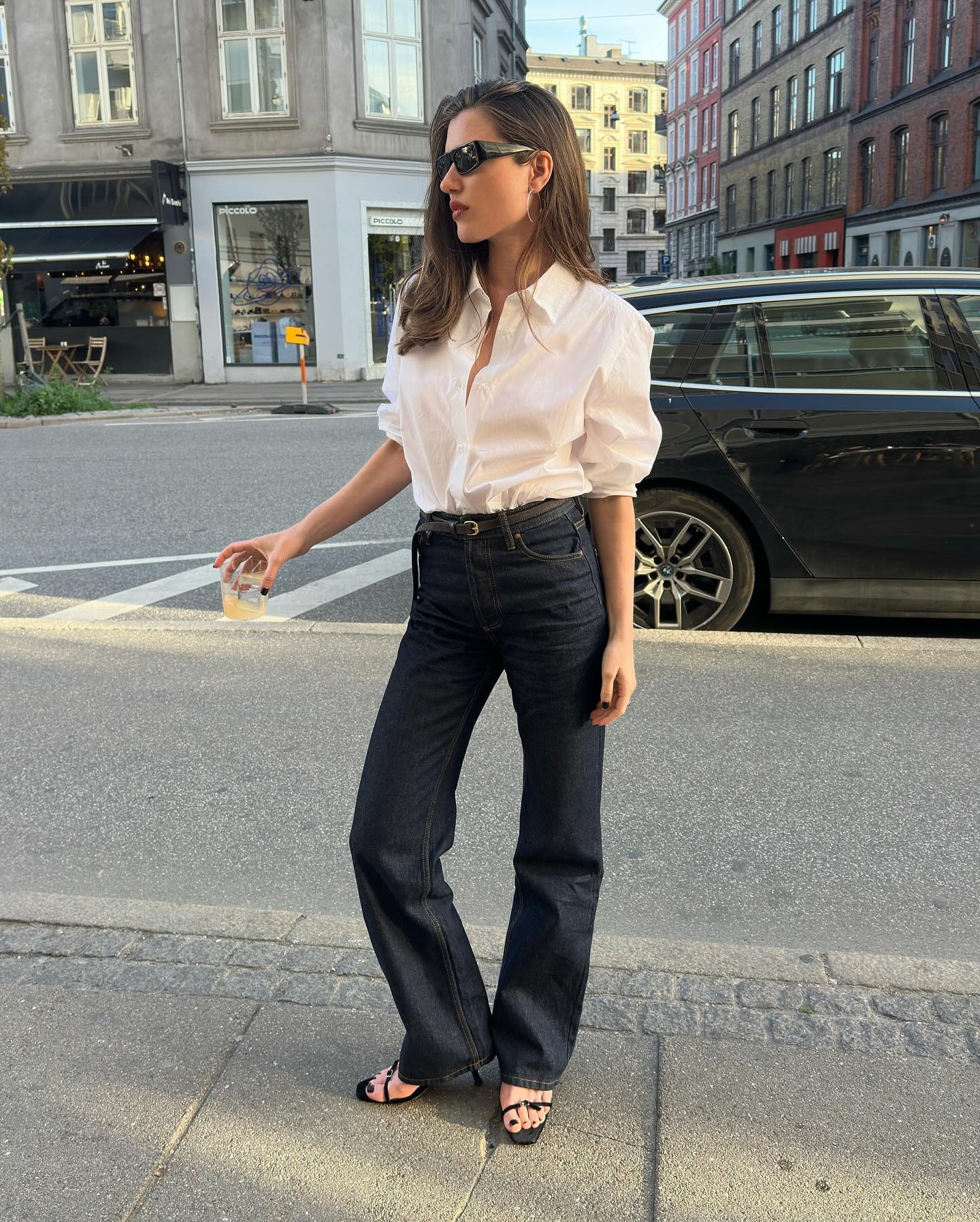 @iliridakrasniqi wearing a white button-down shirt with flare jeans and sandals.