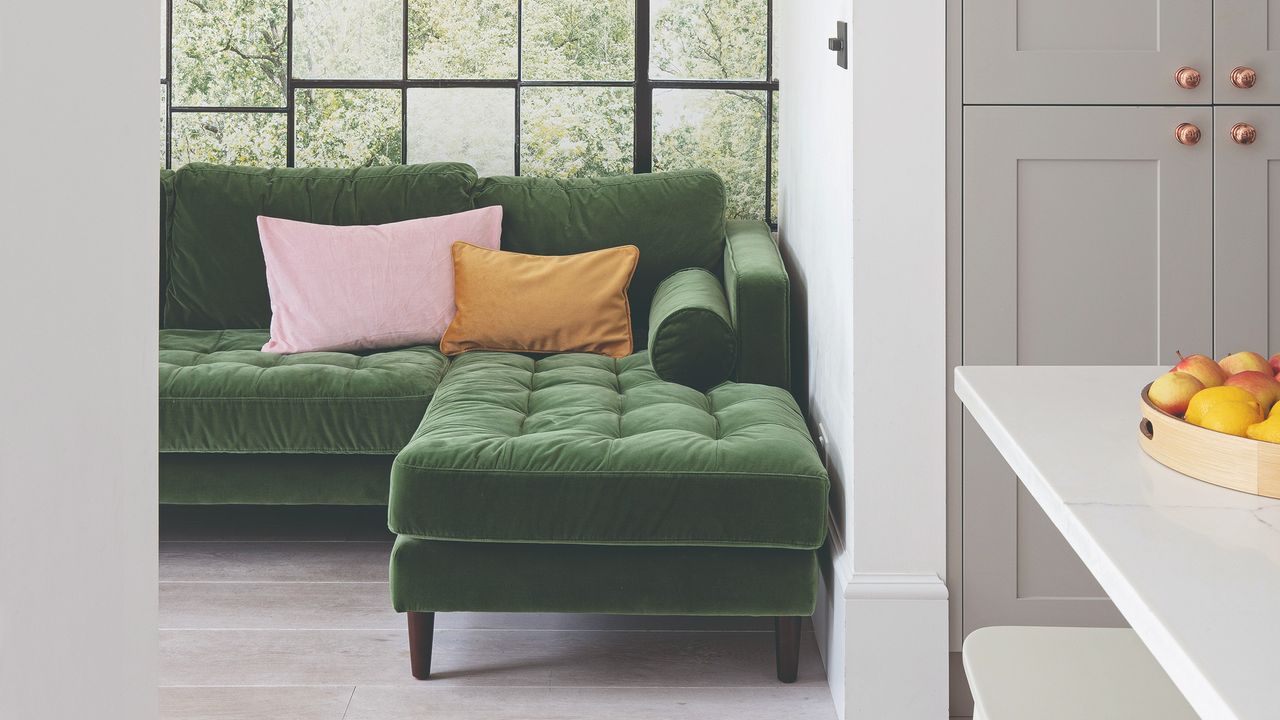 Green velvet corner sofa in a living room with large windows