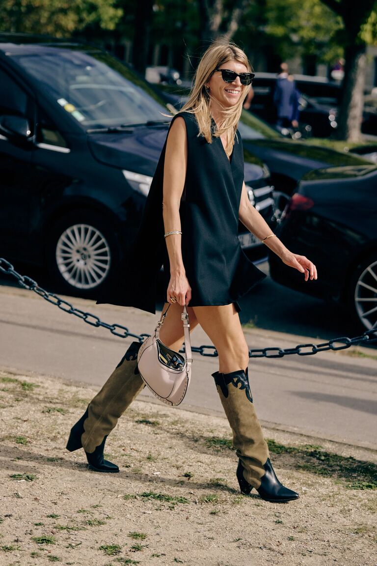 a woman at paris fashion week wearing a black dress and brown suede western boots