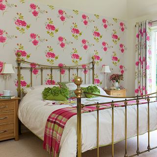 bedroom with floral wall golden bed with designed cushions wooden drawer and cream colour flooring