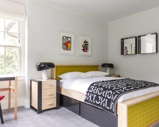 A boys bedroom with yellow bed, blue sheets and patterned black and white wallpaper
