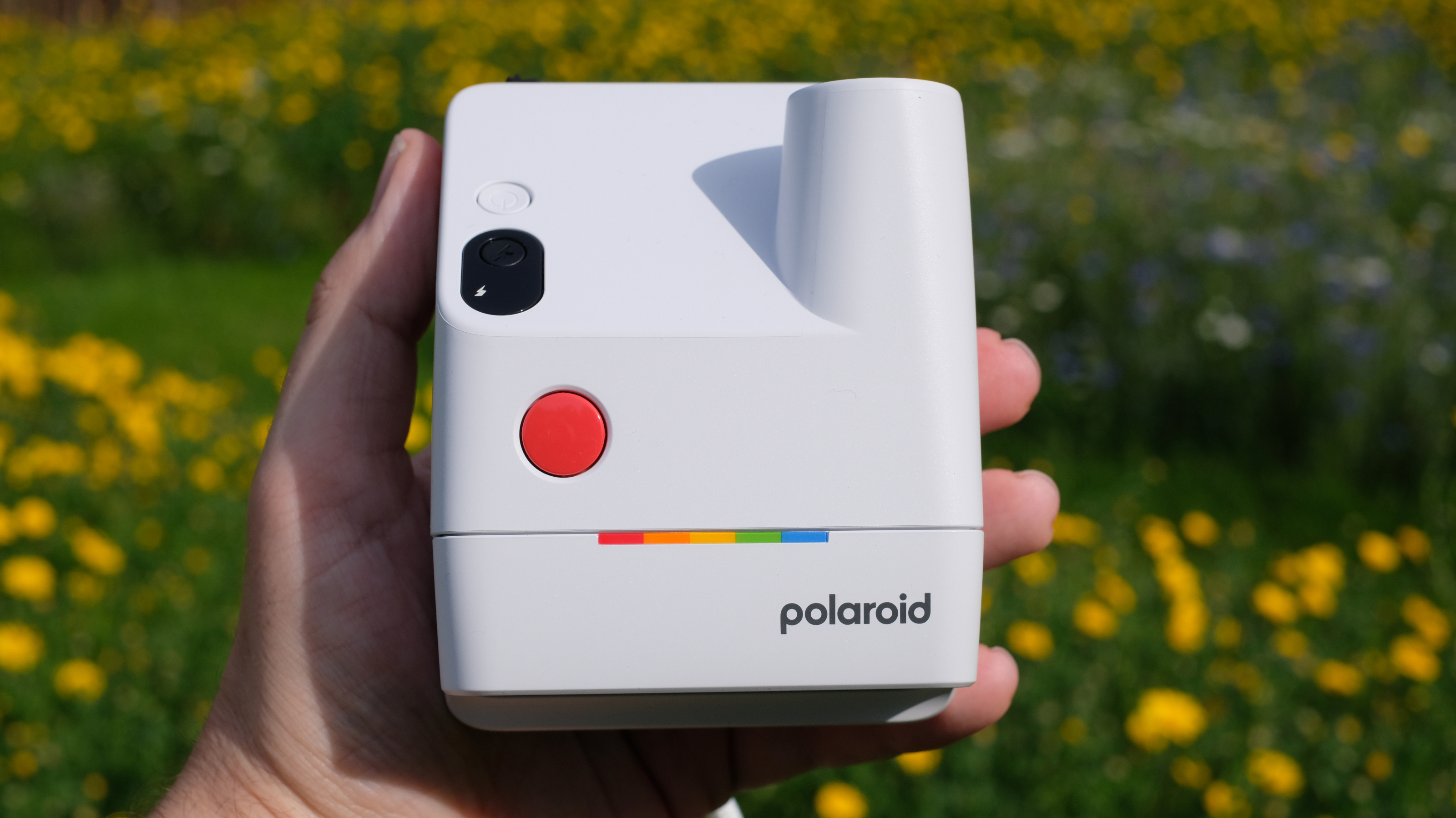 Photograph of man's hand holding Polaroid Go Gen 3 camera in white, with the top visible showing logo, red shutter button, power button and shot counter display