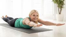 A woman doing superman stretch exercise on a yoga mat in a brightly lit room
