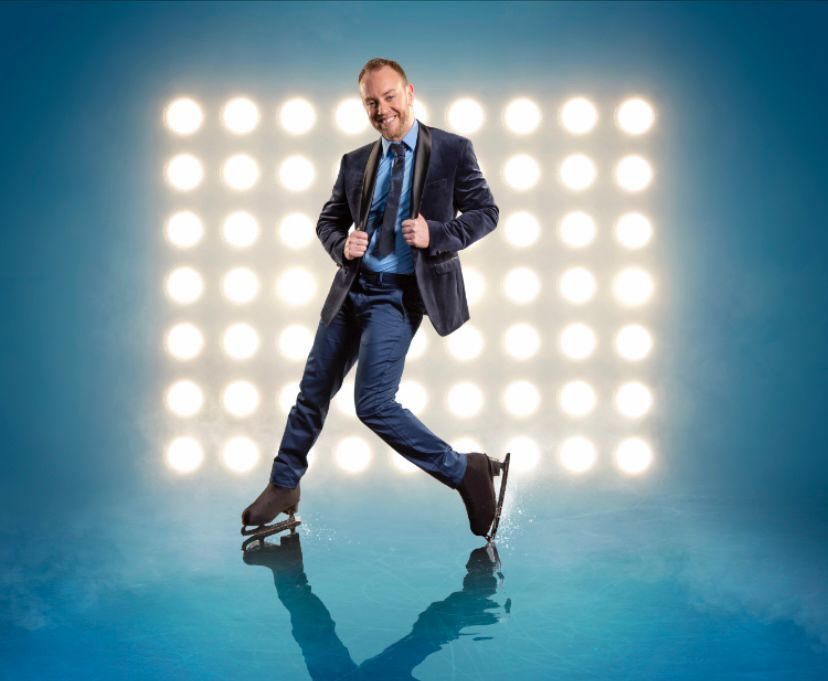 A posed shot of Dancing On Ice&#039;s Dan Whiston wearing a black blazer, light blue shirt with a dark blue tie, dark blue trousers and his ice skates, in front of a 9x7 grid of spotlights pointed at the camera