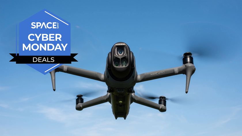 A black quadcopter is hovering in front of blue skies with the space.com logo in the top left corner.