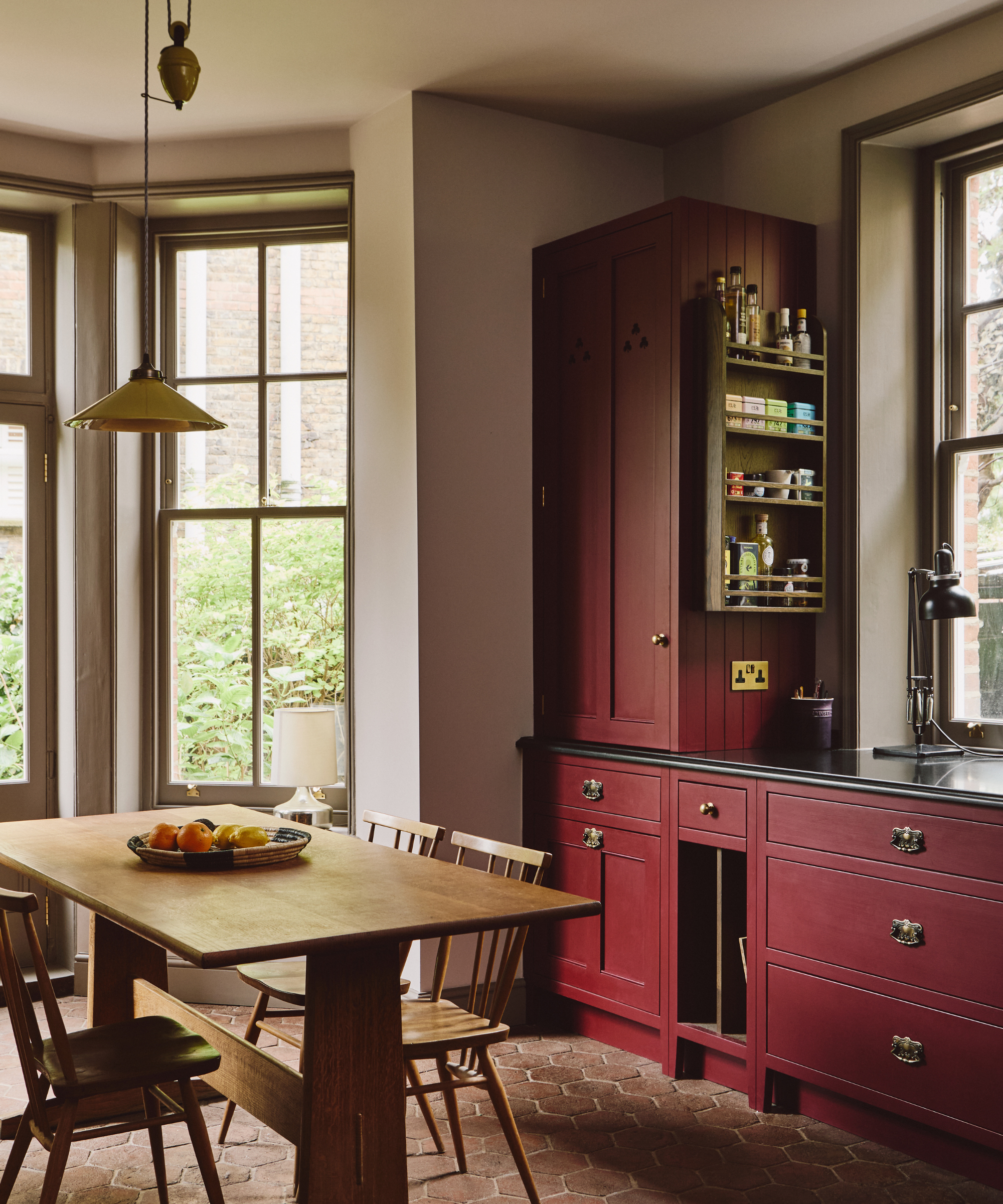 Crimson-painted kitchen area with large, rustic windows and a wooden dining set.