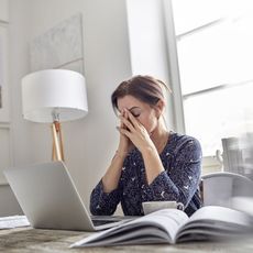 Tired, stressed businesswoman at laptop with head in hands