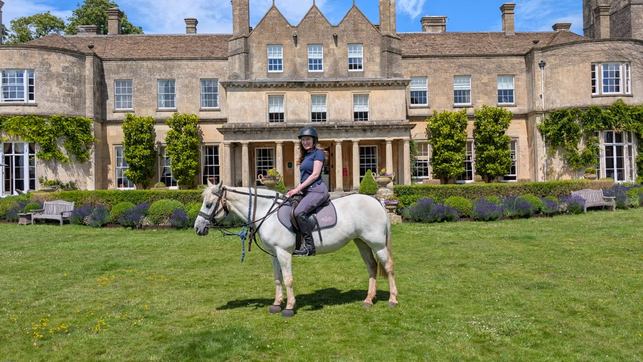 Kristin Contino sitting on a white horse in front of the Lucknam Park hotel