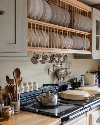 A rustic kitchen with a range oven, a plate rack, and mugs on undermount hooks