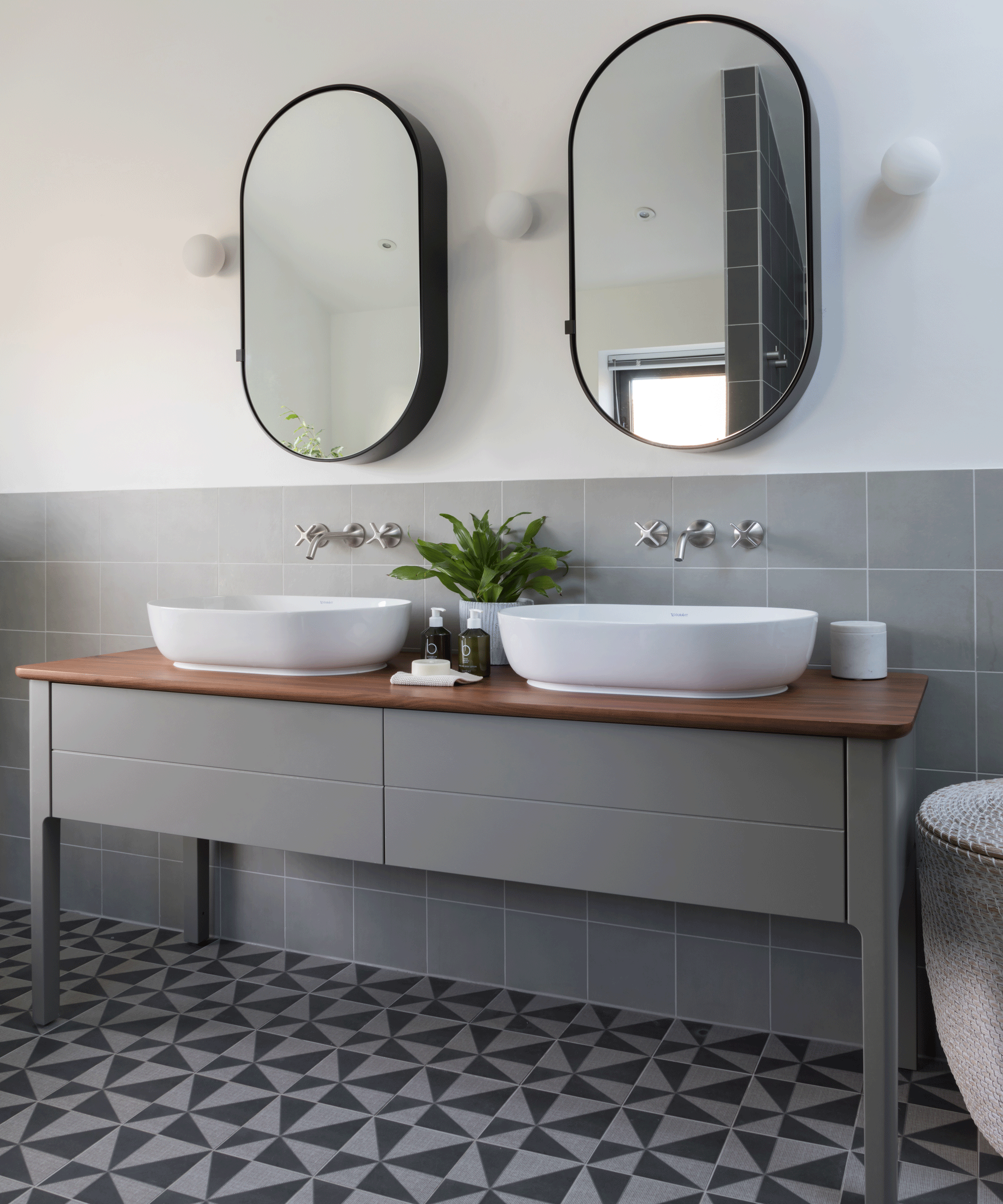 An example of bathroom vanity ideas showing a gray bathroom double vanity unit with white sinks and a gray and black mosaic tiled floor