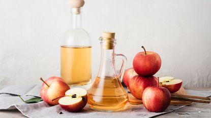 Red apples next to a bottle of apple cider vinegar.