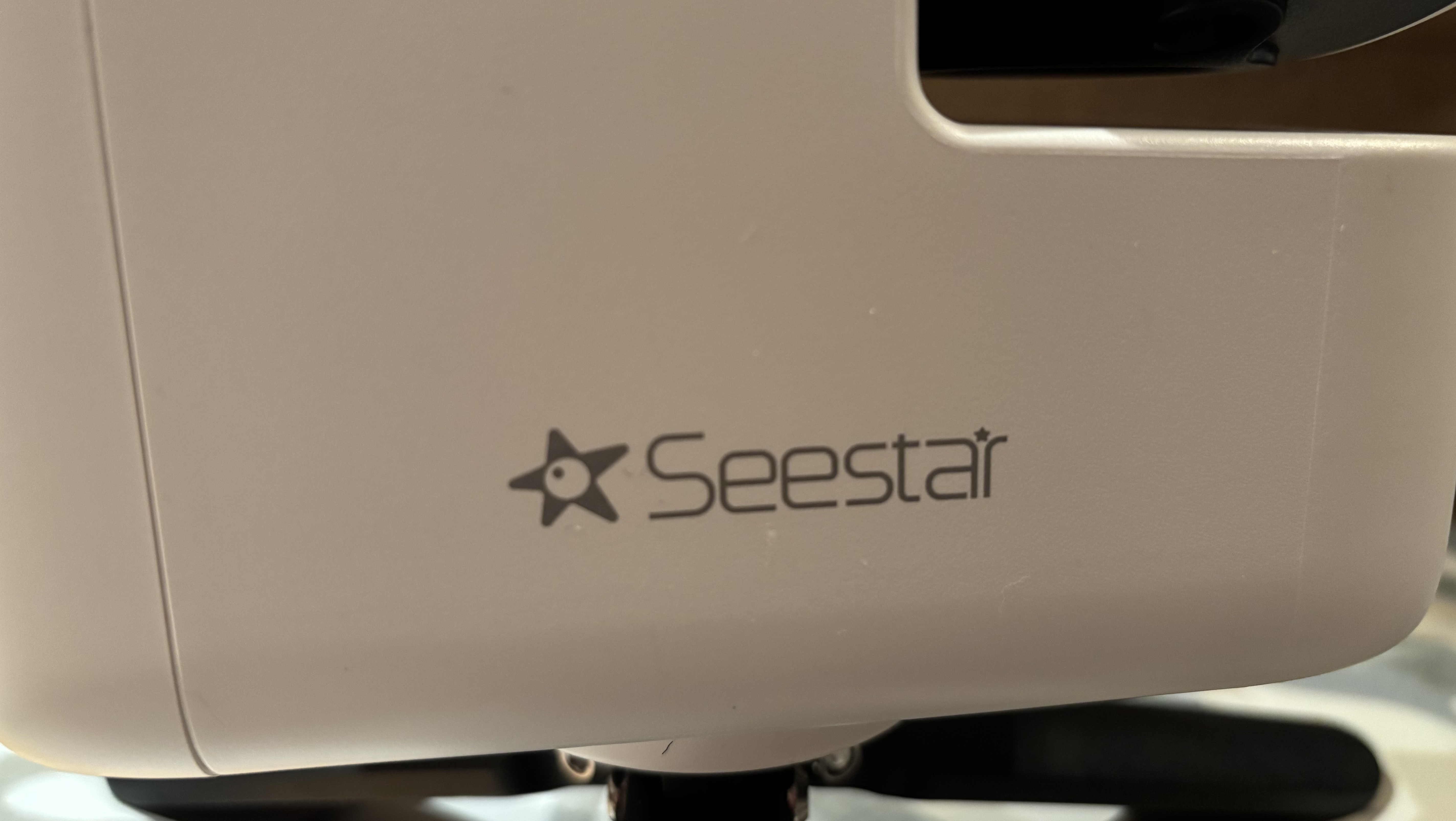 A close up of the Seestar logo on a white telescope - the logo is a dark star with a white circle in the centre and the word "Seestar" to the right of it.