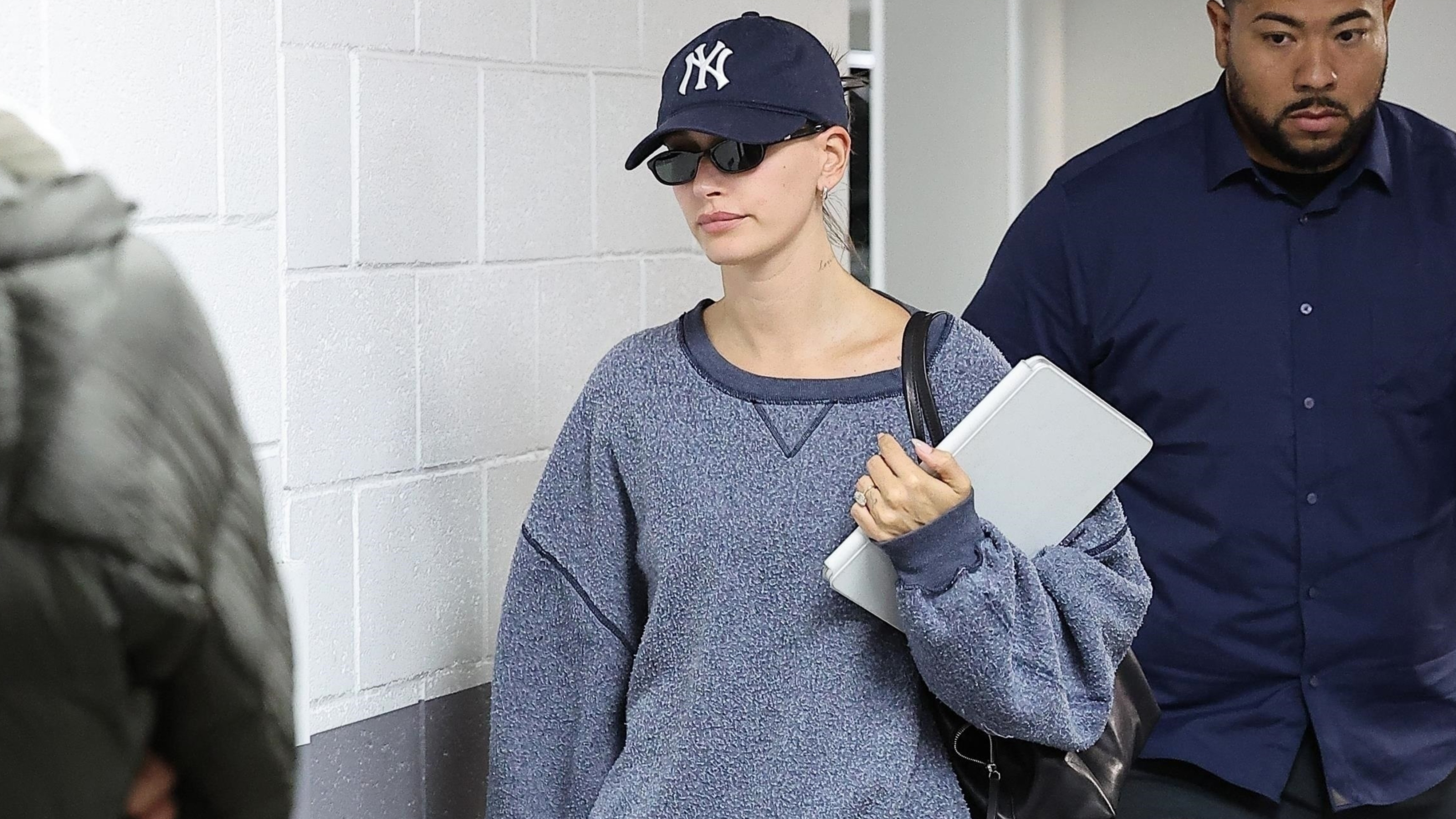 Hailey bieber wears a yankees hat, gray sweatshirts, black shorts, white socks and navy suede miu miu sneakers.