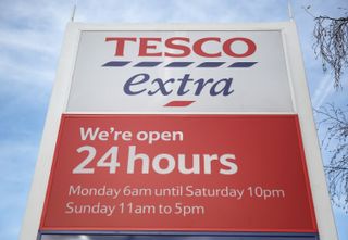 A sign for a Tesco Extra that is open 24 hours