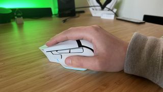 Hand holding Razer Basilisk V3 Pro 35K gaming mouse in a palm grip on a wooden desk