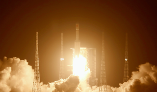 a rocket lifts off in the night. launch towers surround the rocket