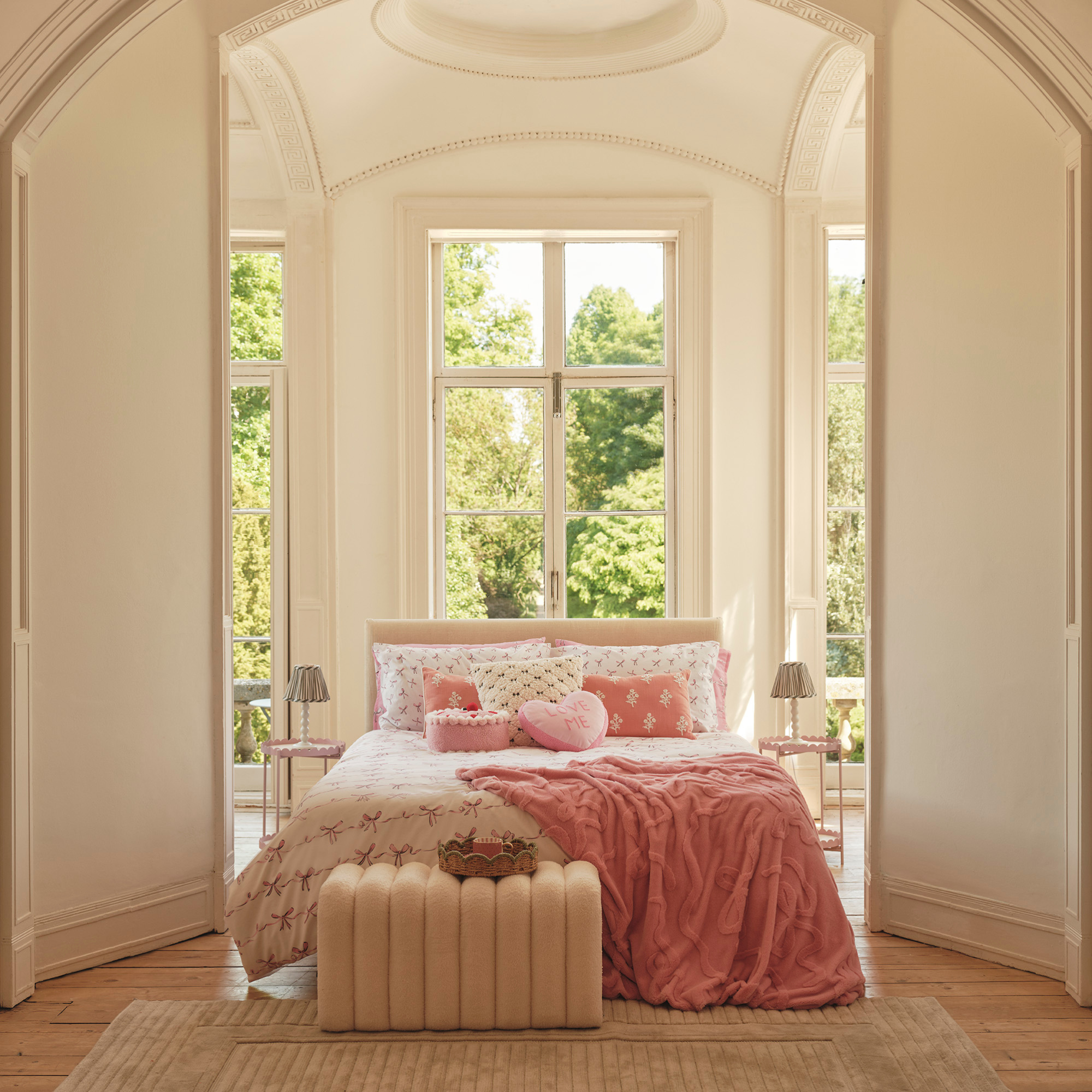 Pink bedd in a large bedroom with high ceilings and huge French doors.