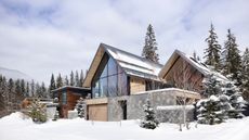 Contemporary A-frame home in snow with forest and mountains