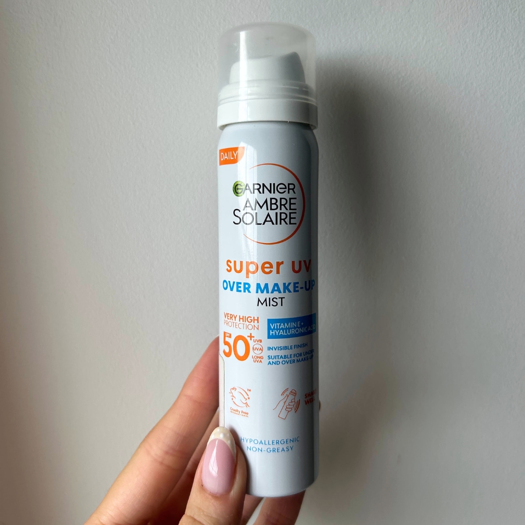 Hand holding bottle of Garnier Ambre Solaire Super UV Over Makeup Sun Protection Face Mist SPF50+