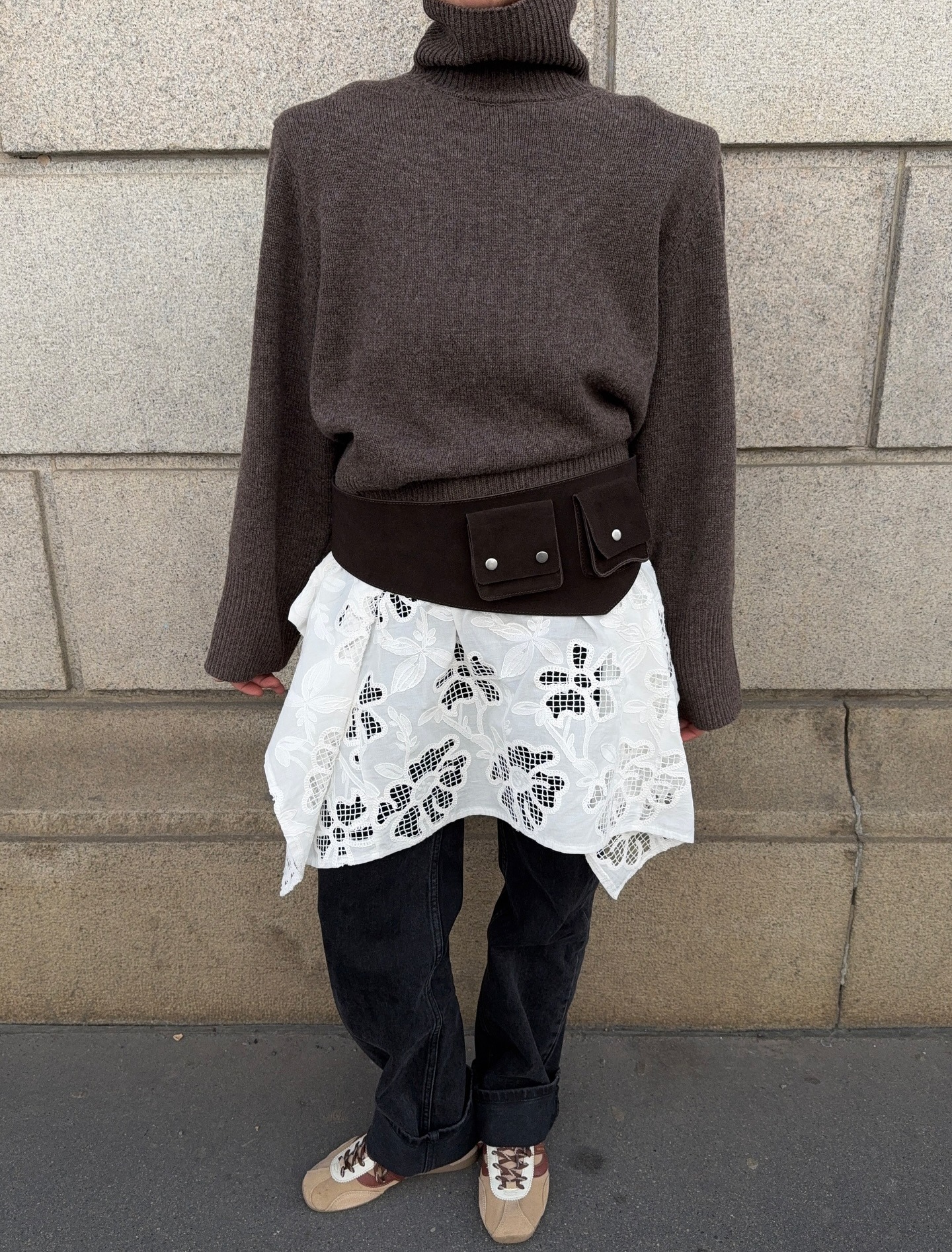 Influencer Dina Hansen is wearing a lace dress over jeans, a brown turtleneck, a suede belt, and a woven leather bag.