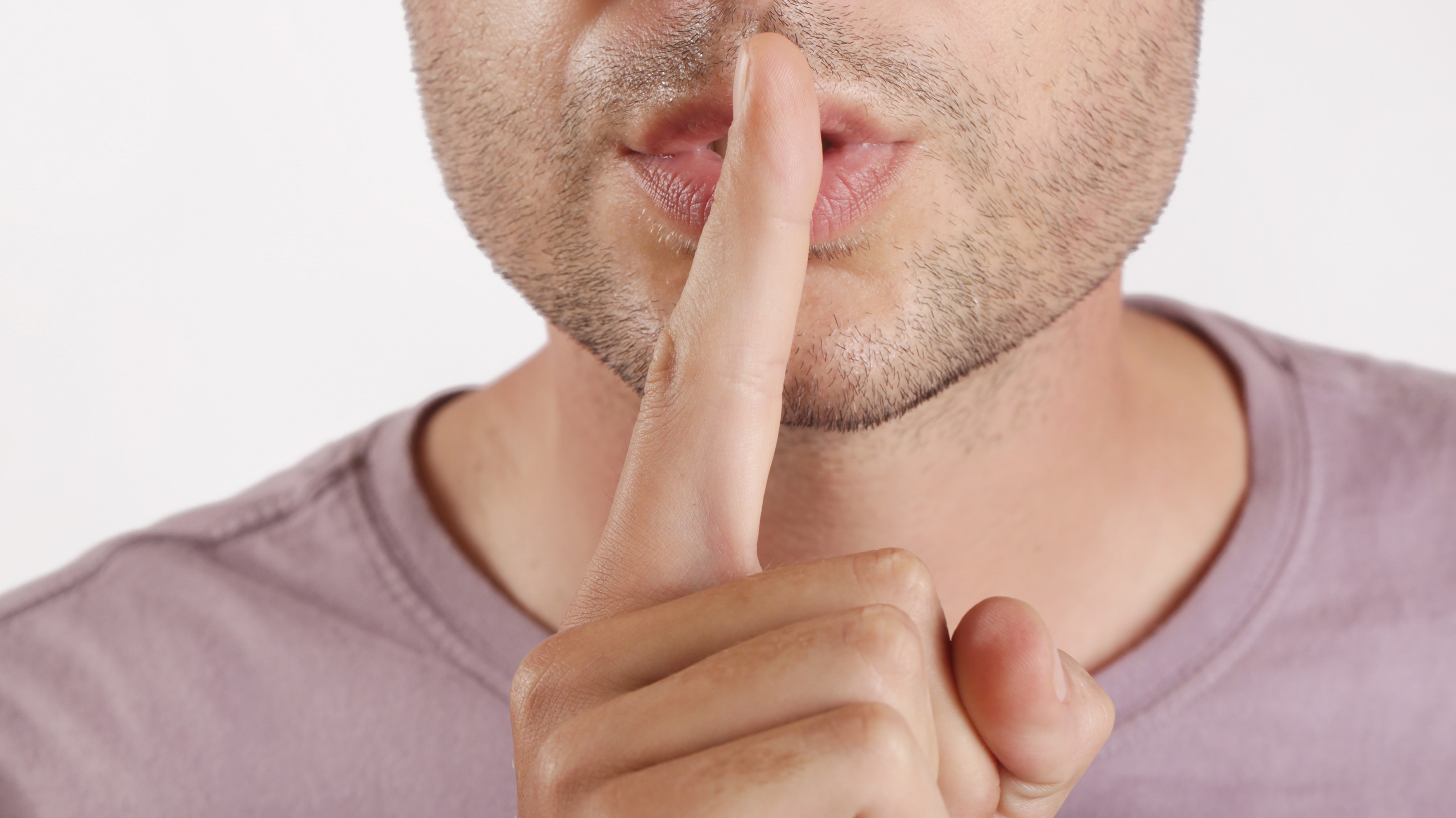 A man puts his finger to his lips as if to say, 