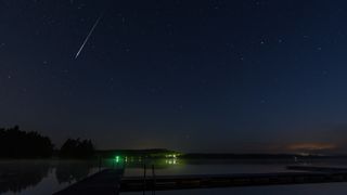 A meteor streaks overhead above a lake.